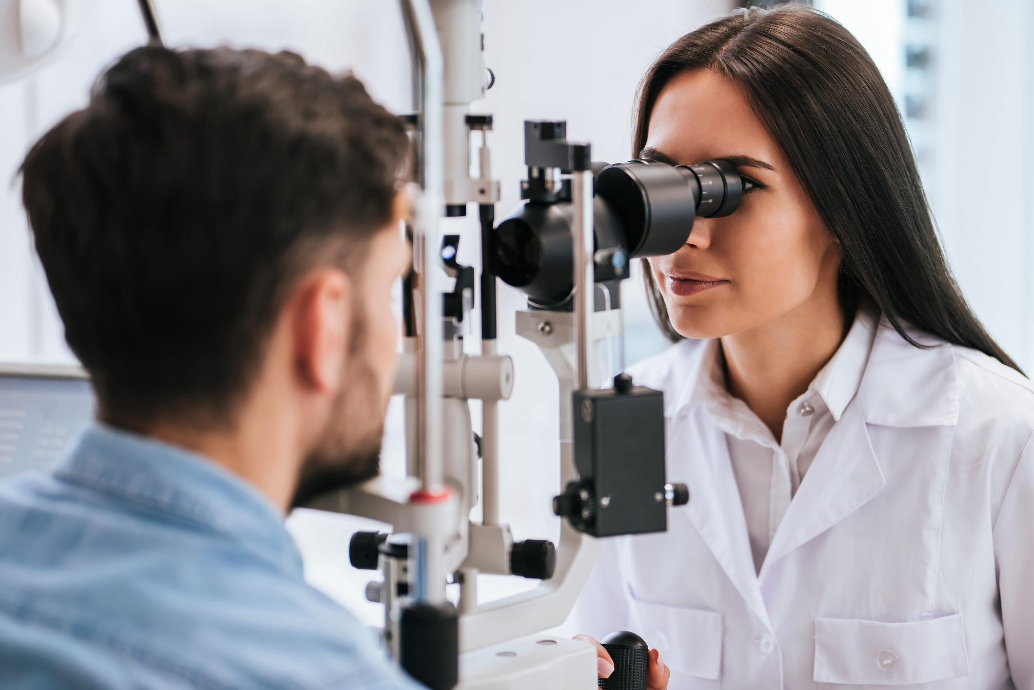 Attractive female doctor  ophthalmologist is checking the eye vision of handsome young man in modern clinic. Doctor and patient in ophthalmology clinic.
